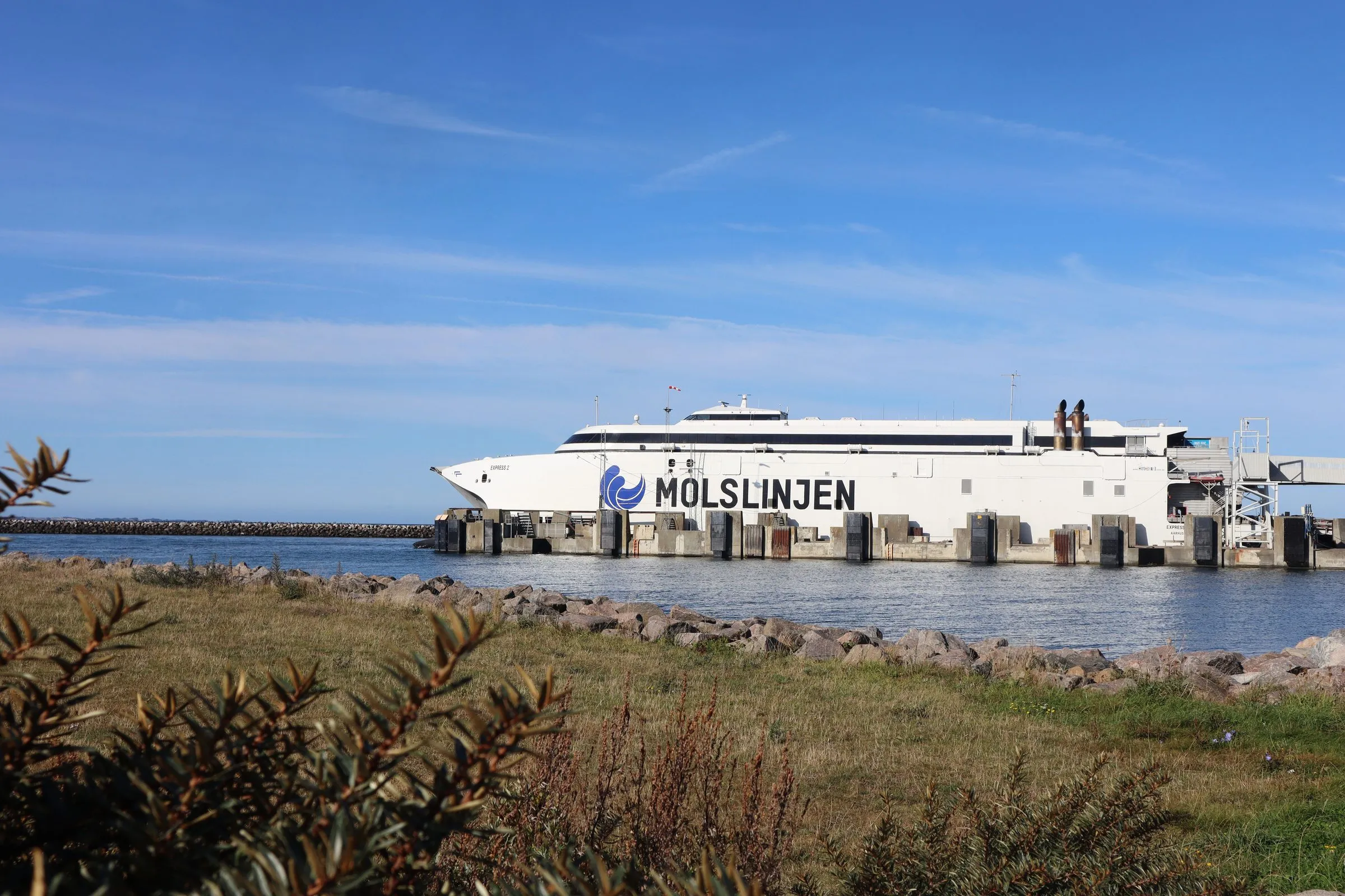 En vit katamaran från Molslinjen ligger vid piren i Odden under klar himmel