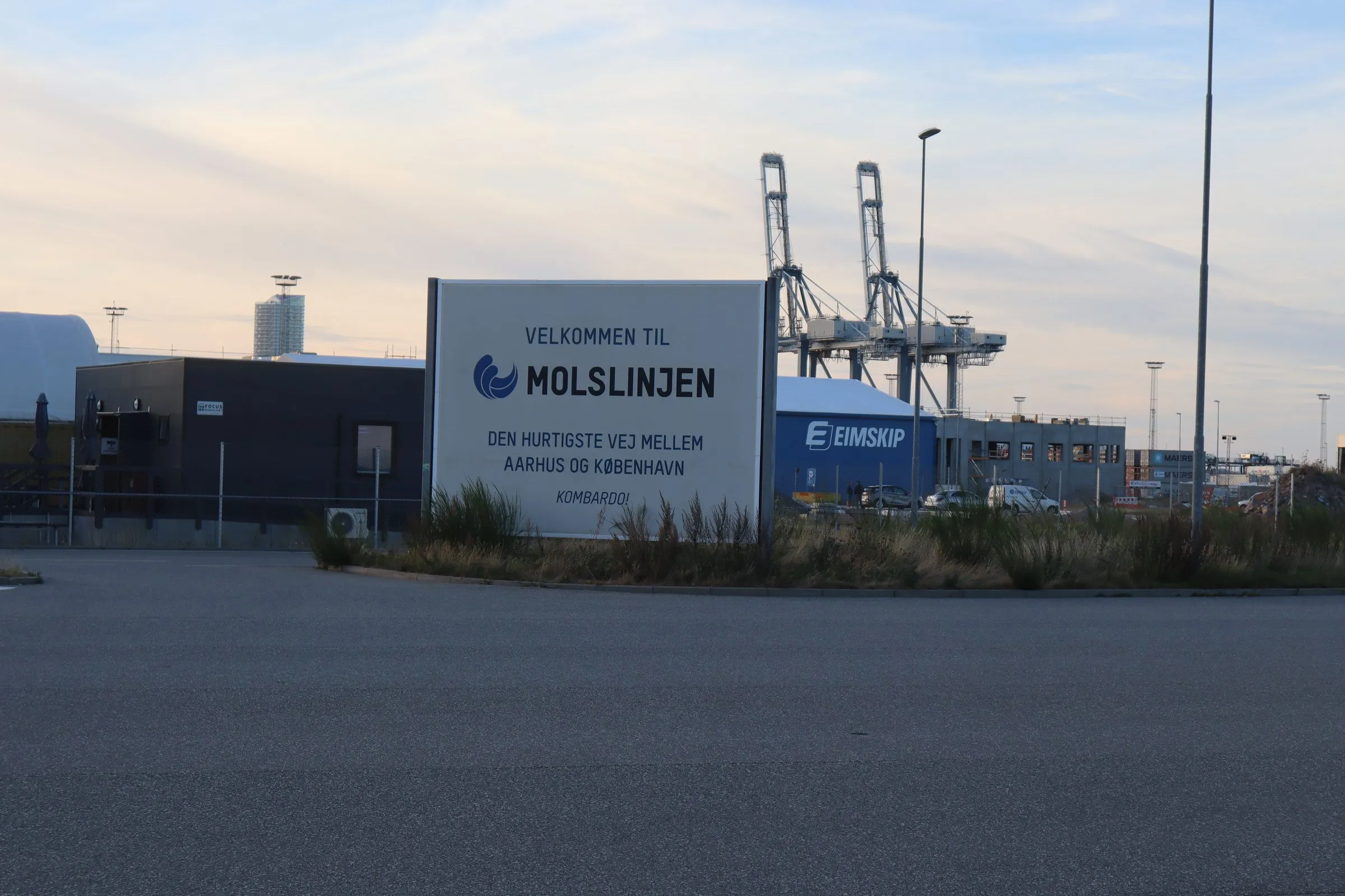 De toerit naar de Molslinjen-terminal in Aarhus met welkomstbord en containerkranen erachter