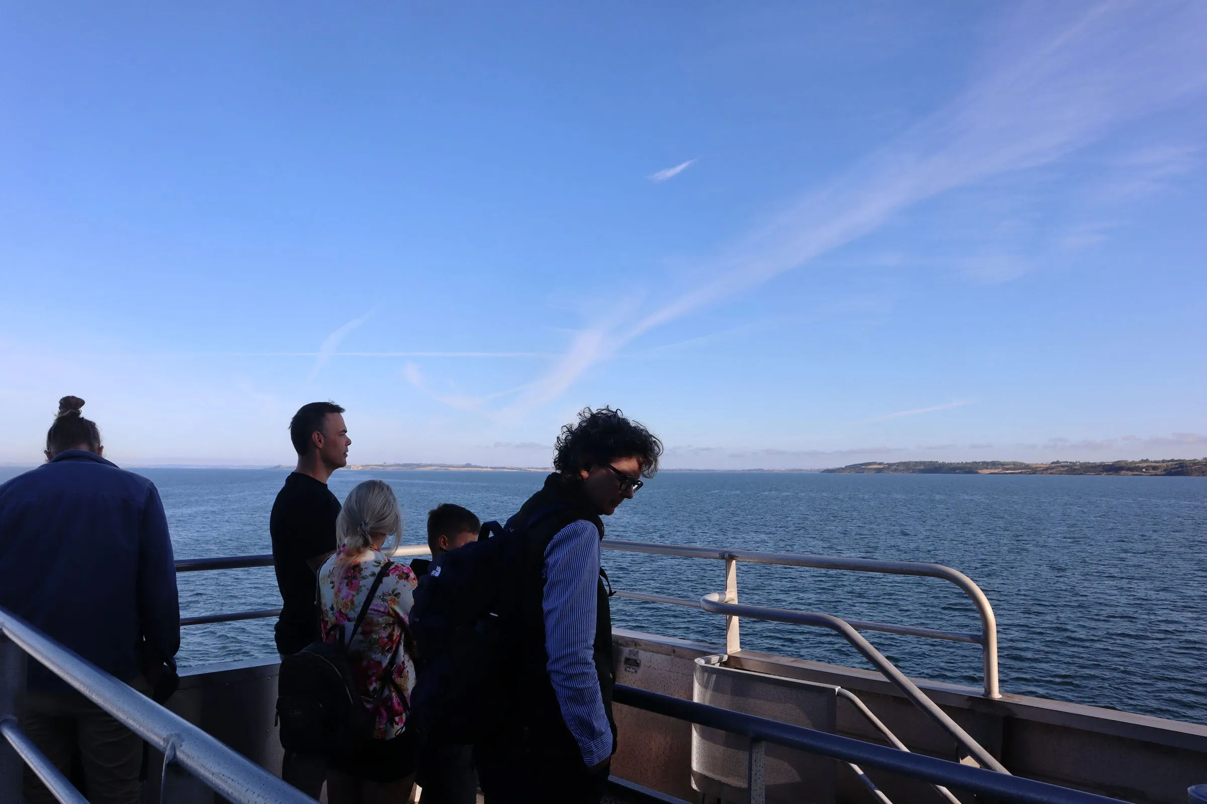 Passagerer står ved rælingen på det åbne dæk og ser ud over havet